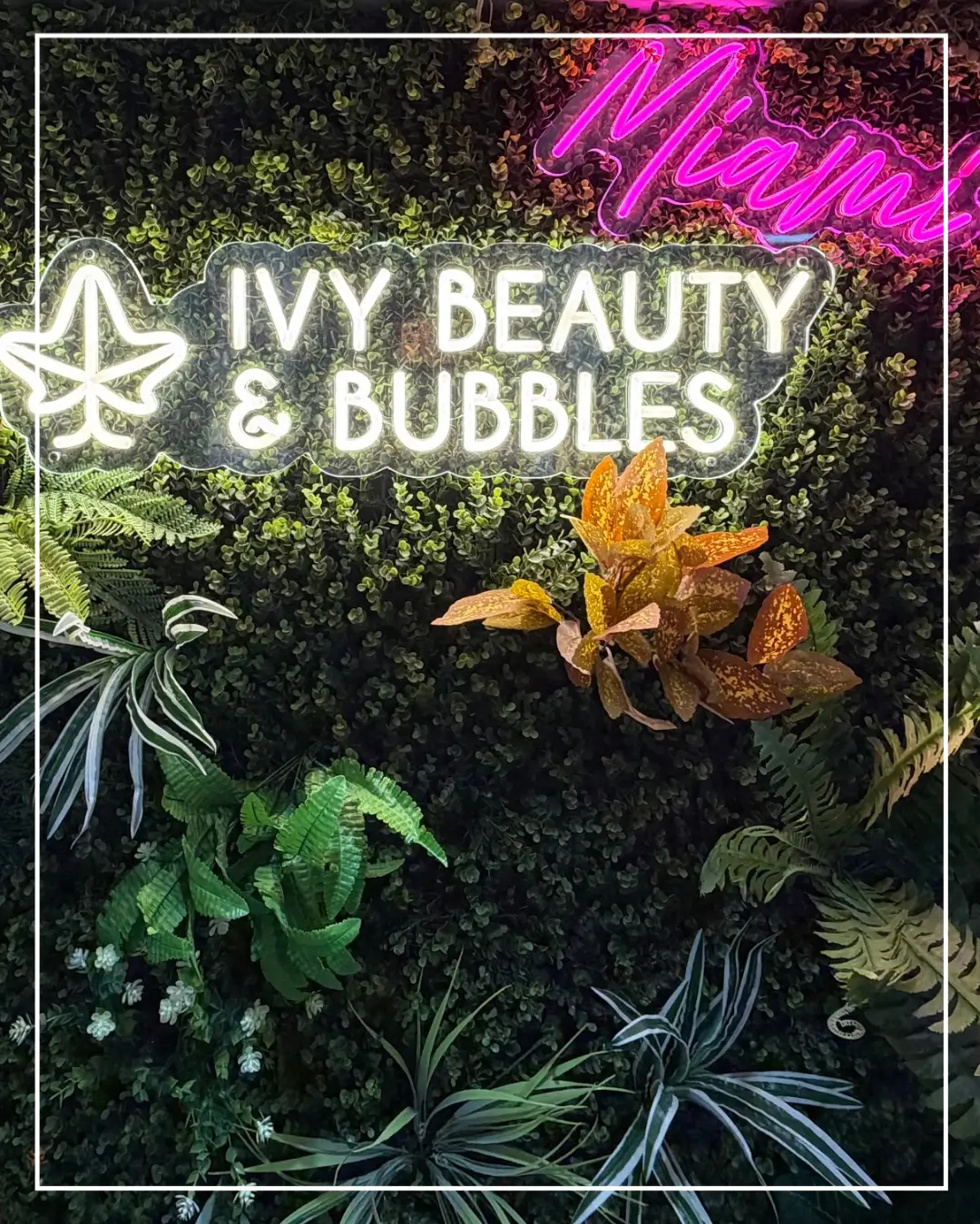 Plant wall with the illuminated IVY Beauty & Bubbles Dubai salon sign.